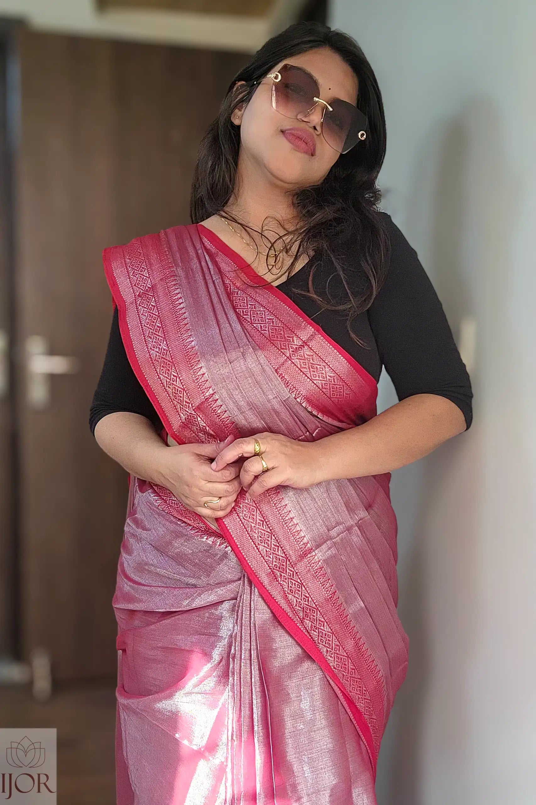Woman wearing a Lavender Pure Tissue Cotton Saree with Rich Red Border with a black blouse against a neutral wall.
