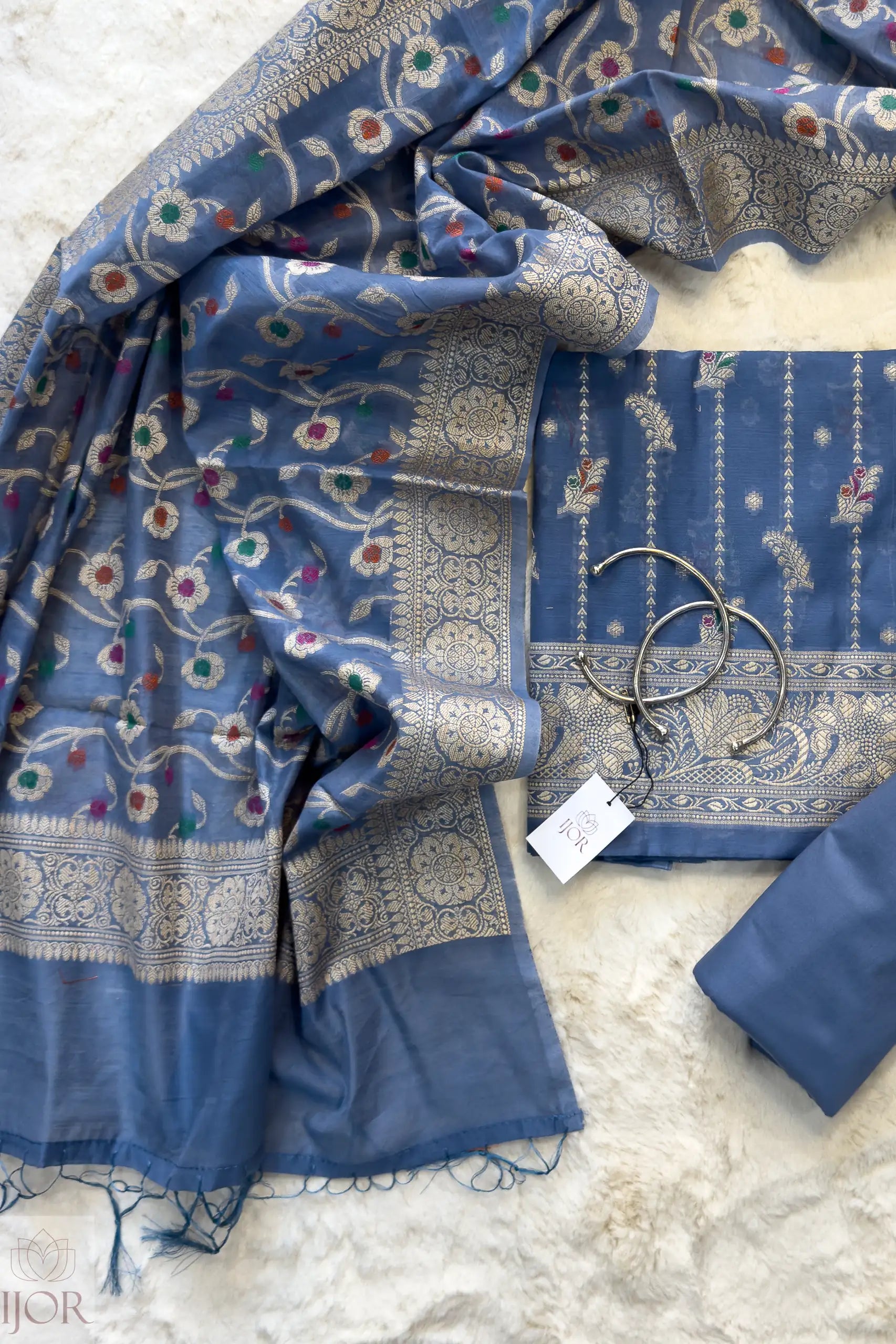 Dusty Blue Muga Silk in Minakari work Unstitched Suit with a tag on a light gray background