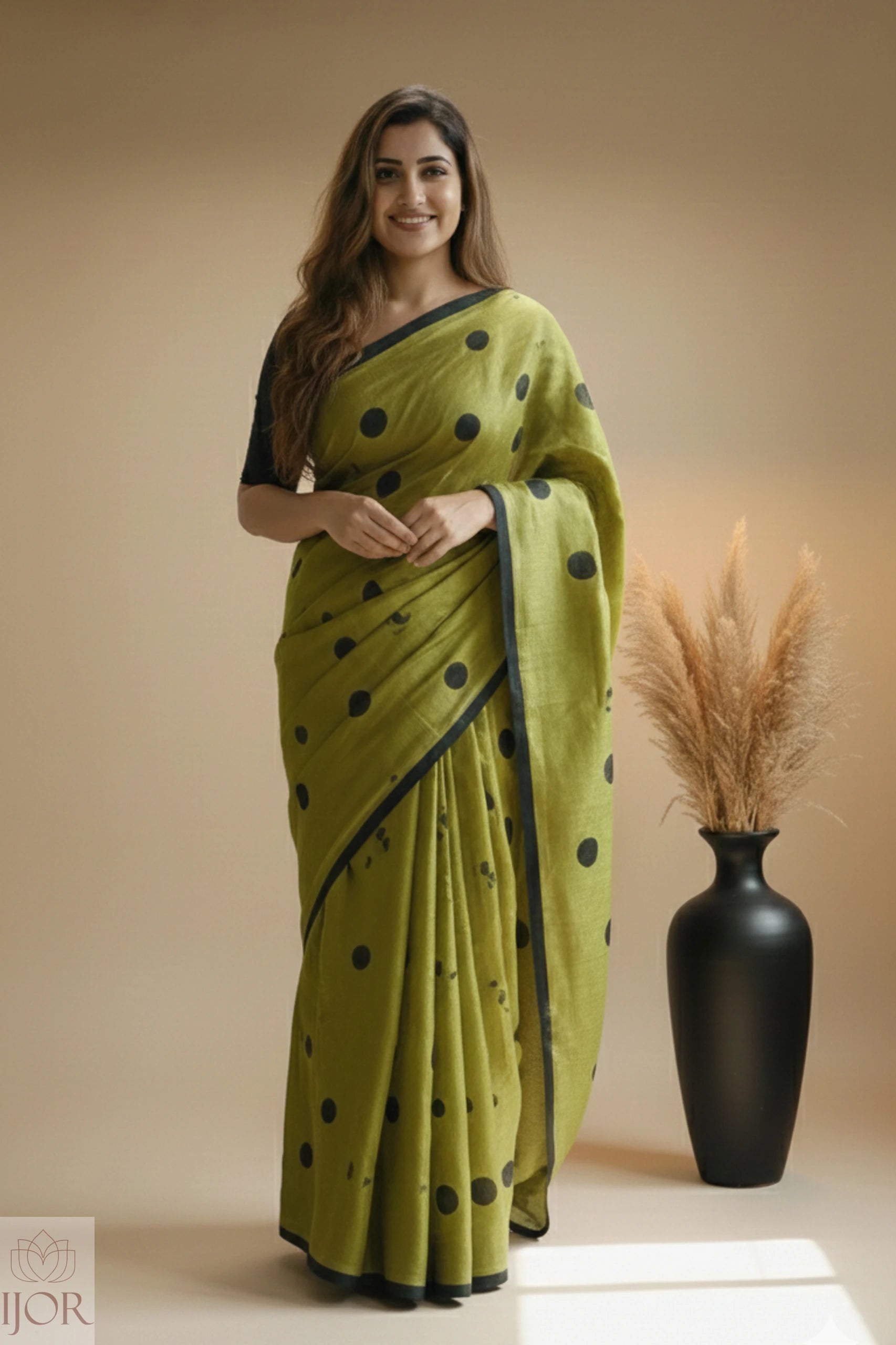 Pure Khadi Cotton Olive Green Saree with black polka and beautiful Tassels standing next to a black vase with dried plants on a beige background