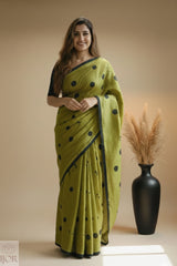 Pure Khadi Cotton Olive Green Saree with black polka and beautiful Tassels standing next to a black vase with dried plants on a beige background