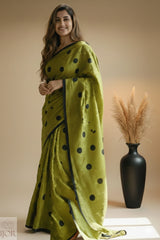 Pure Khadi Cotton Olive Green Saree with black polka and beautiful Tassels, standing against a beige background with a vase of dried plants.