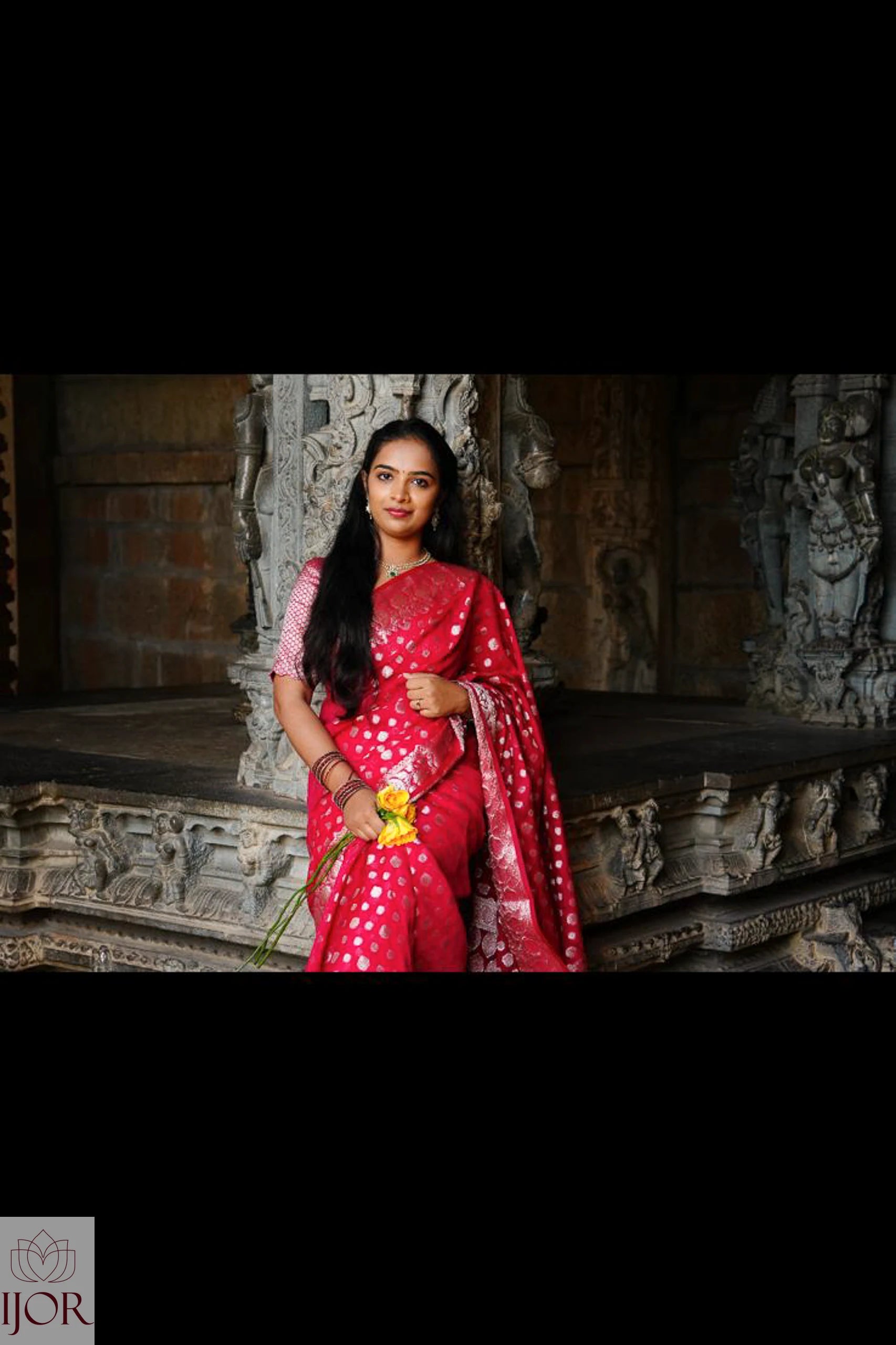 Nandini Yallareddy in Banarasi Soft Georgette Silk Red Saree standing in front of stone carvings