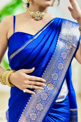 Woman wearing a blue saree with a white border, holding her hand up.