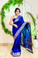Woman in a blue saree with a decorative border standing in front of a decorative arch.