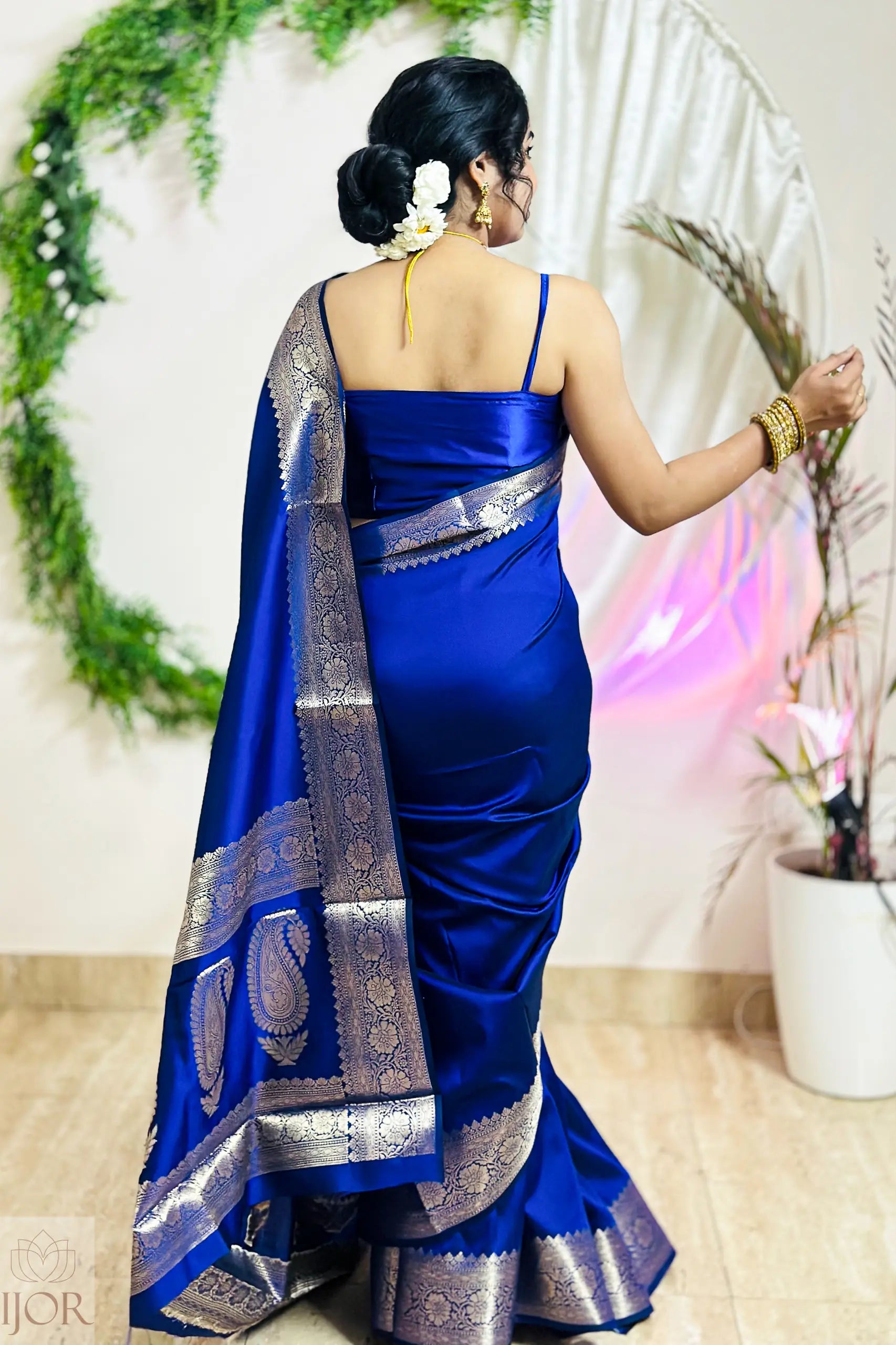 Woman wearing a blue saree with silver patterns, standing indoors.