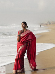 Divya Darshini ft. in Banarasi Soft Semi Katan Silk Saree Red standing on a beach with ocean waves in the background