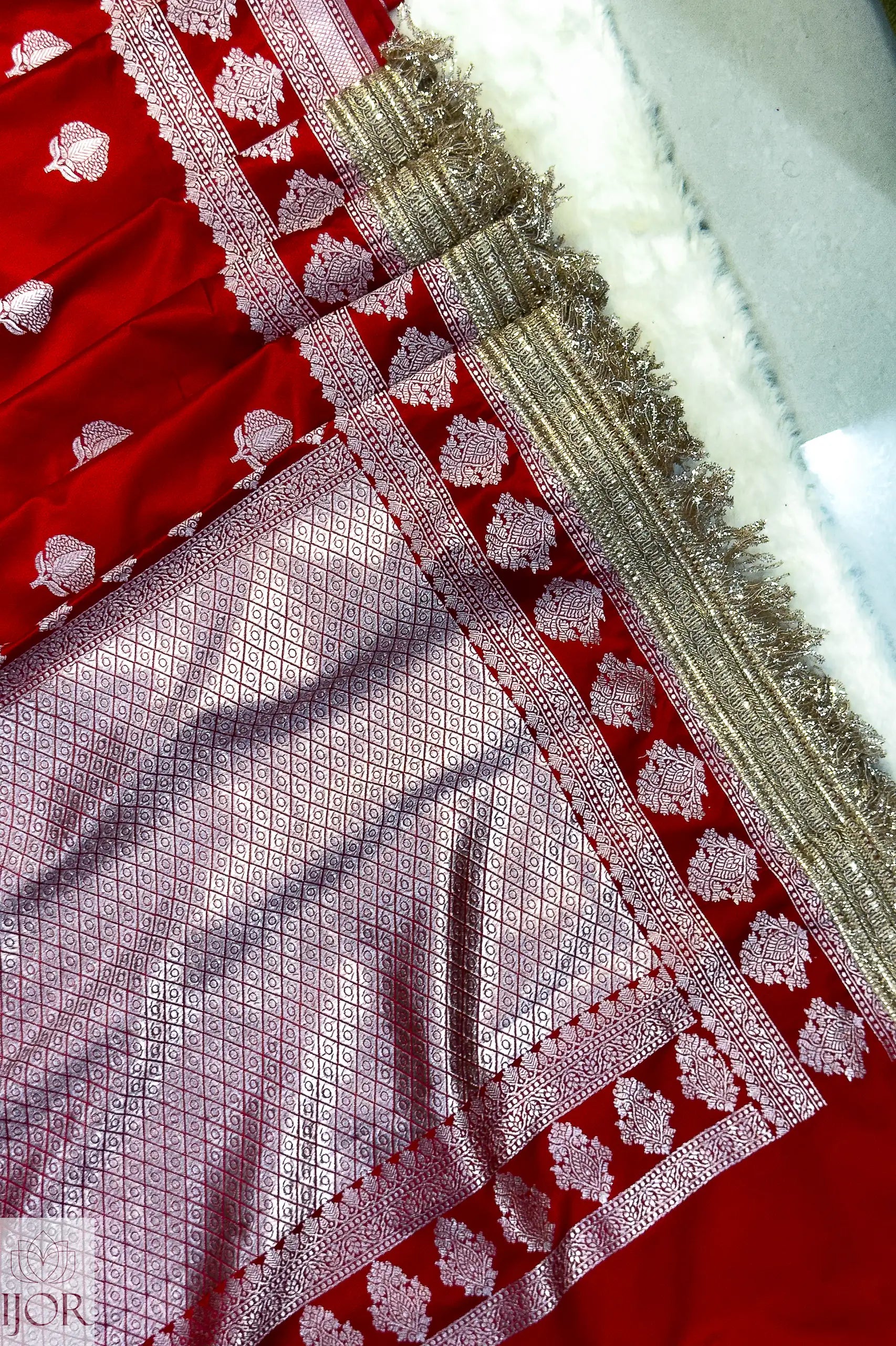Close-up of a Red Mashru Silk Saree with Maharani Lace patterns and gold trim.