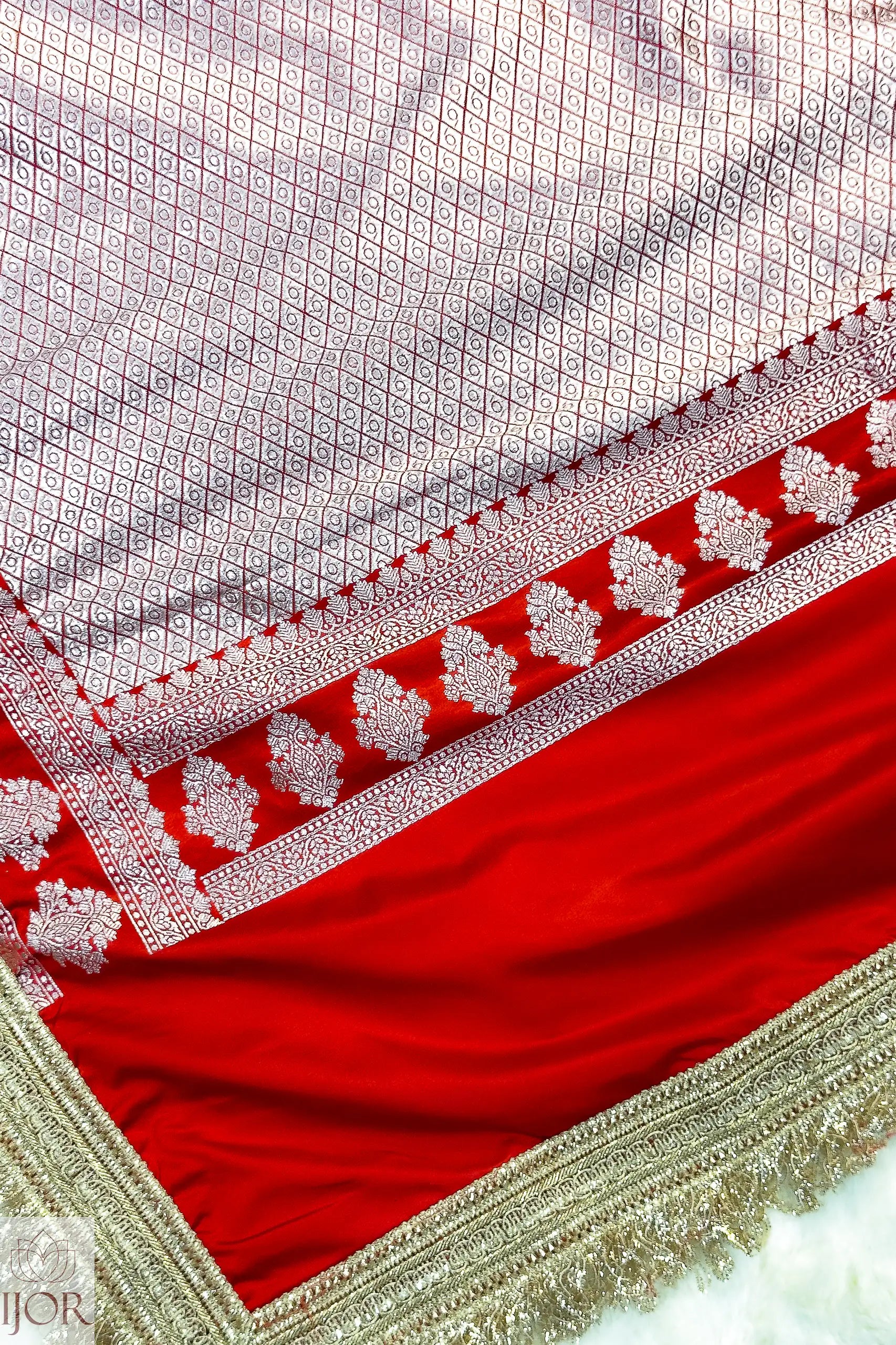 Close-up of a Red Mashru Silk Saree with Maharani Lace on a light pink background.