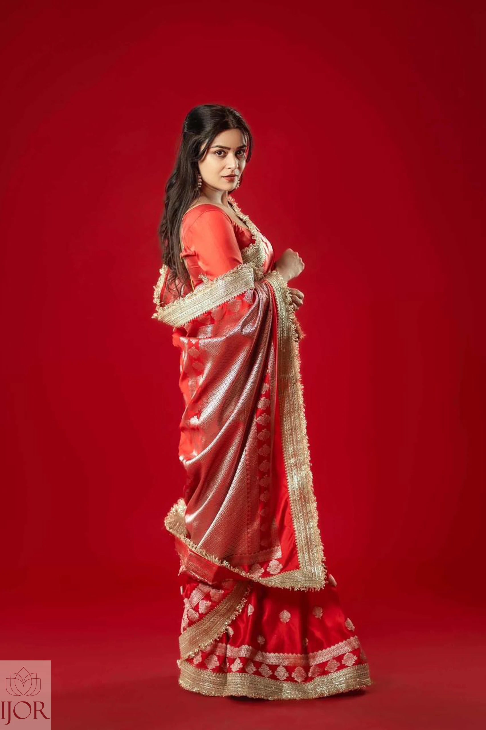 Woman wearing a Red Mashru Silk Saree with Maharani Lace against a red background