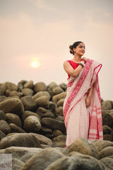Woman in a Dhonkhali Red and White Pure Cotton Check saree standing among rocks with a sunset in the background