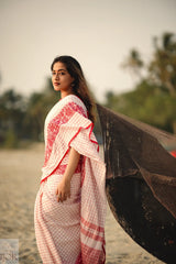Woman in a Dhonkhali Red and White Pure Cotton Check saree standing next to a fishing net on a beach.