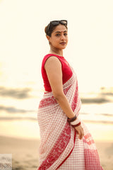 Woman in a Dhonkhali Red and White Pure Cotton Check saree standing by a body of water.