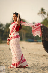 Woman in a Dhonkhali Red and White Pure Cotton Check saree standing on a beach with palm trees in the background