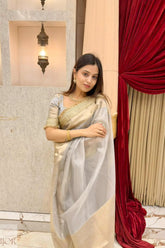 Woman in a Banarasi Silver Grey Tissue Silk Saree standing in front of a red curtain and light fixture.