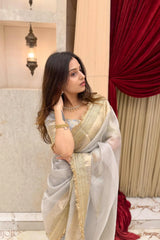 Woman in a Banarasi Silver Grey Tissue Silk Saree with gold and white design, standing indoors.