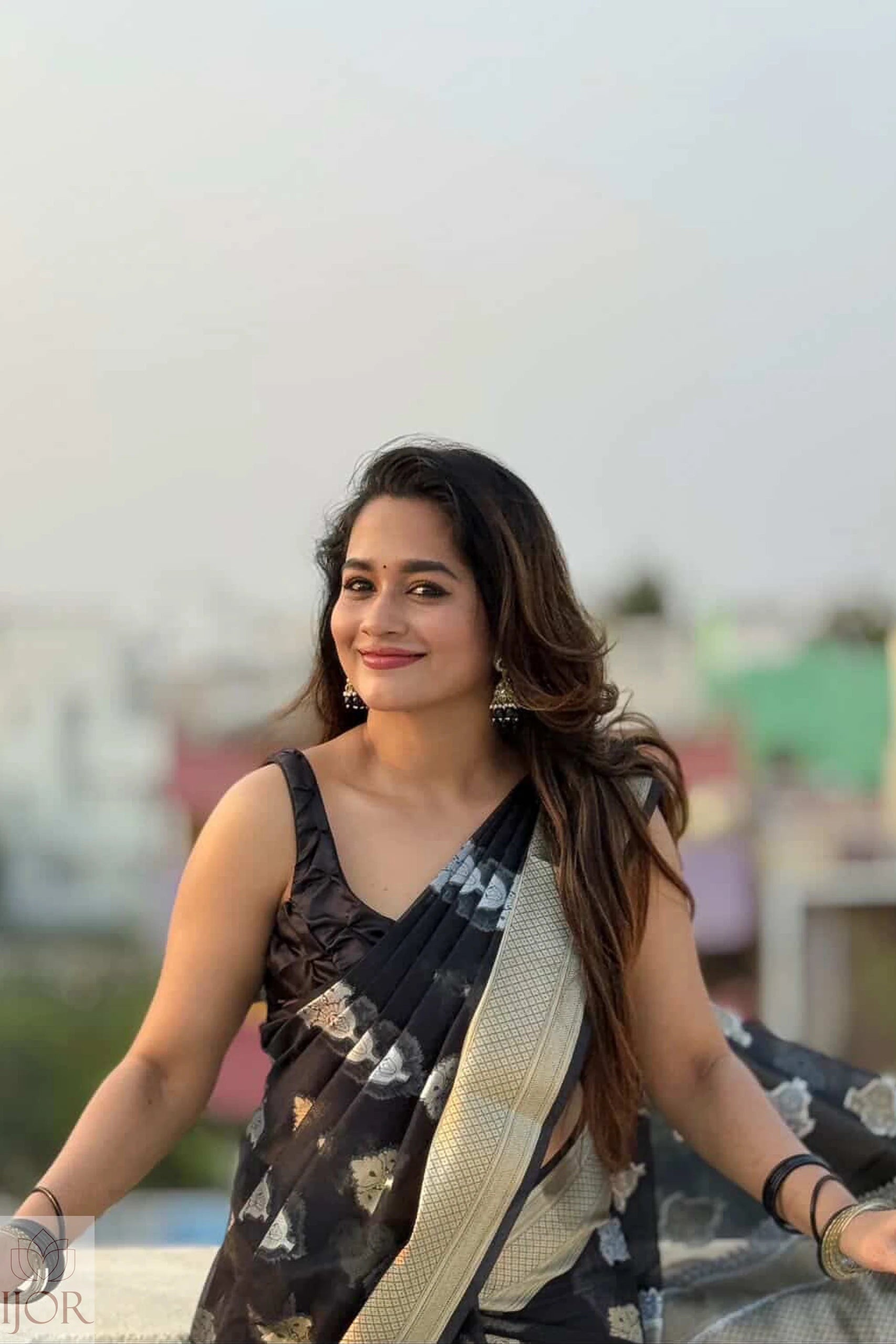 Kavya in a Kora Orgenza Silk Black saree with floral patterns against a blurred outdoor background
