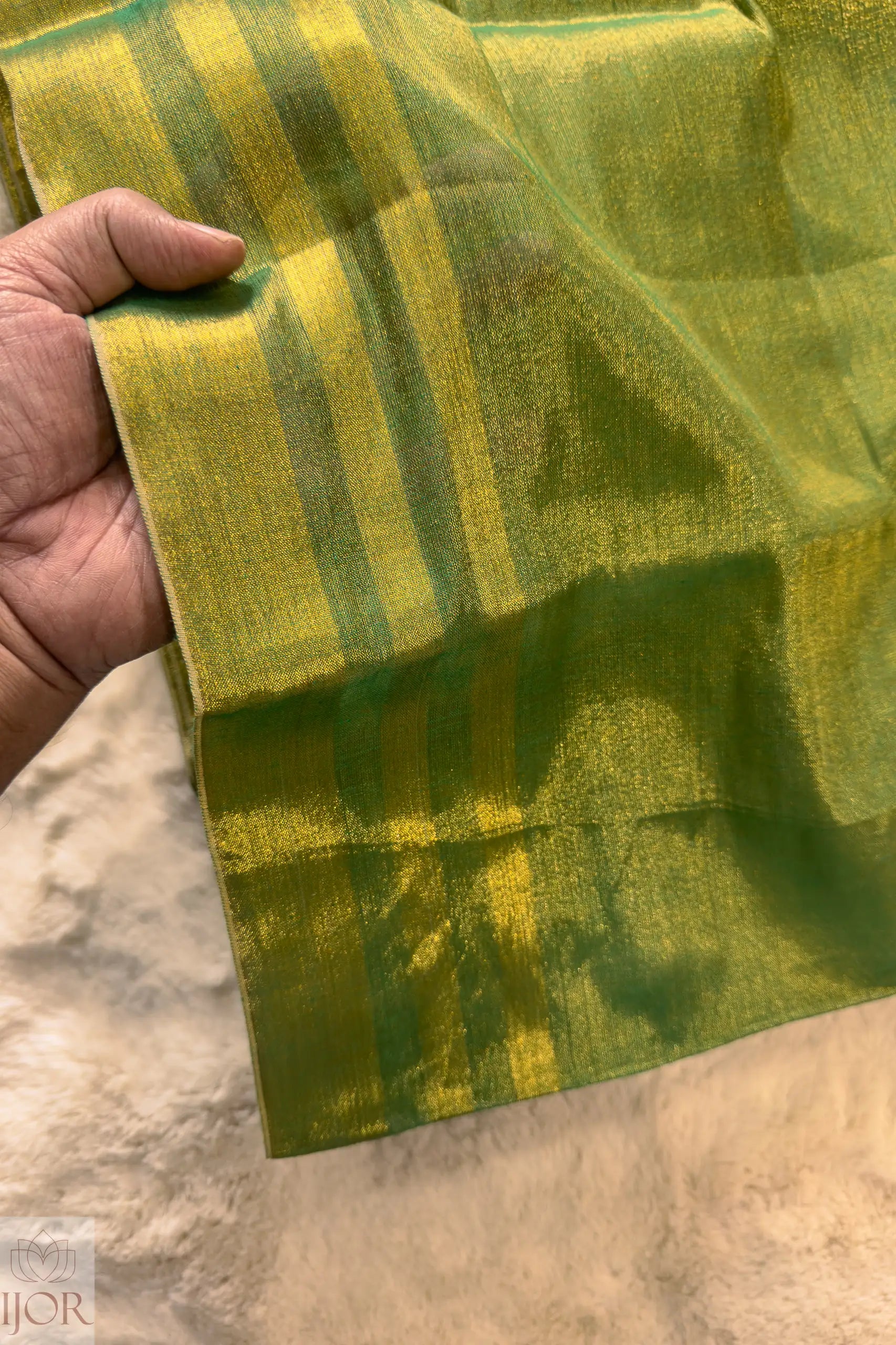 Green Golden Zari Pure Tissue Cotton Saree held by a hand on a beige background