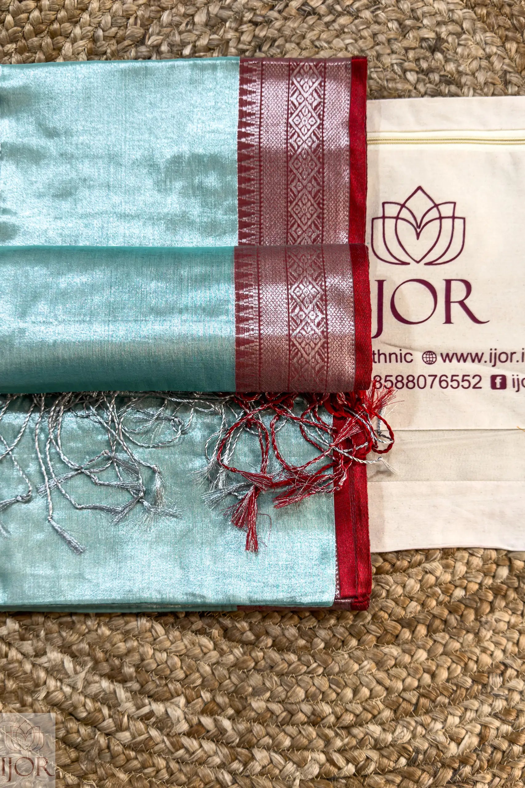 Sea Foam Pure Tissue Cotton Saree with Rich Red Border on a textured surface, featuring the 'IJOR' brand.
