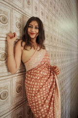 Woman in a patterned Banarasi Soft Georgette Silk Brown Saree standing against an ornate wall.