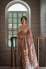 Woman in a Banarasi Soft Georgette Silk Brown Saree standing in a room with a decorative wall and window.