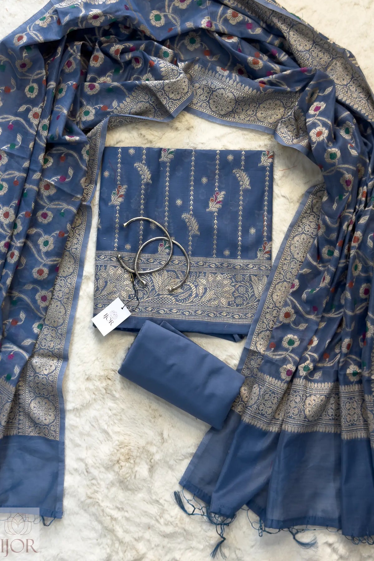Dusty Blue Muga Silk in Minakari work Unstitched Suit with a tag on a light background