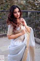 A woman wearing Banarasi Silver Grey Tissue Silk Saree and gold traditional Indian saree, standing outdoors in front of a black metal railing.
