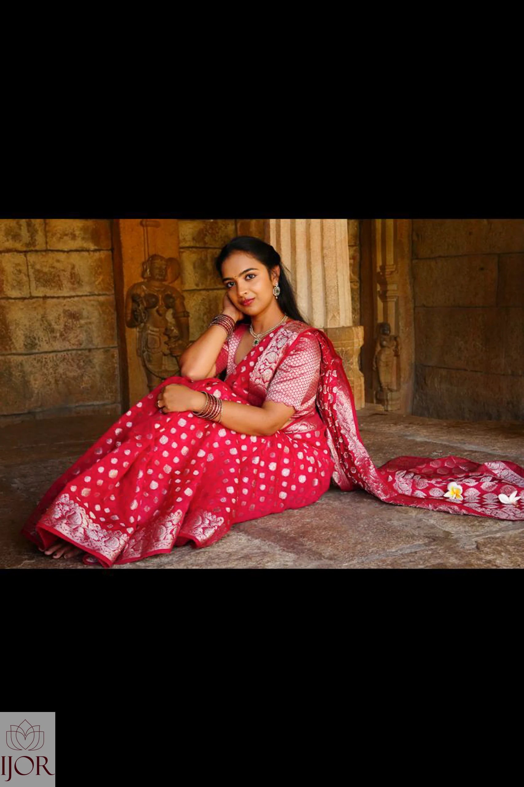 Nandini Yallareddy in Banarasi Soft Georgette Silk Red Saree with silver booti showing entire saree drapped beautifully sitting on a stone floor.