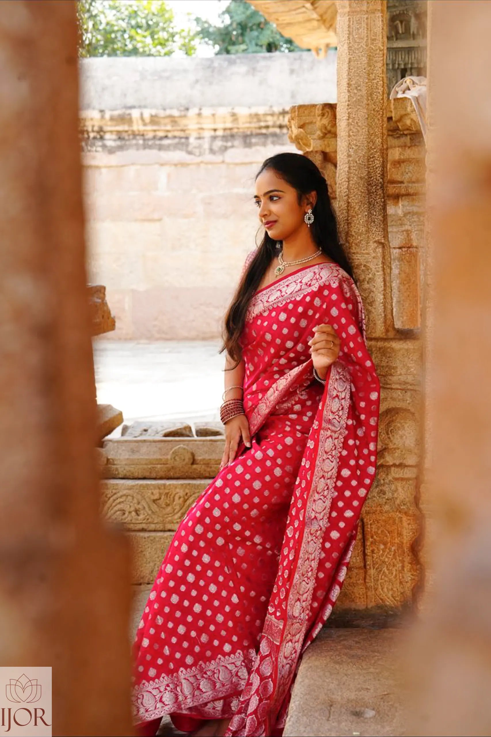 Nandini Yallareddy in Banarasi Soft Georgette Silk Red Saree with silver booti sitting in a temple setting