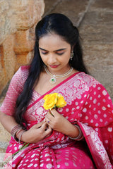 Nandini Yallareddy in Banarasi Soft Georgette Silk Red Saree holding a yellow flower against a stone wall.