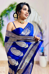 Woman wearing a blue saree with silver patterns, standing indoors with a blurred background.