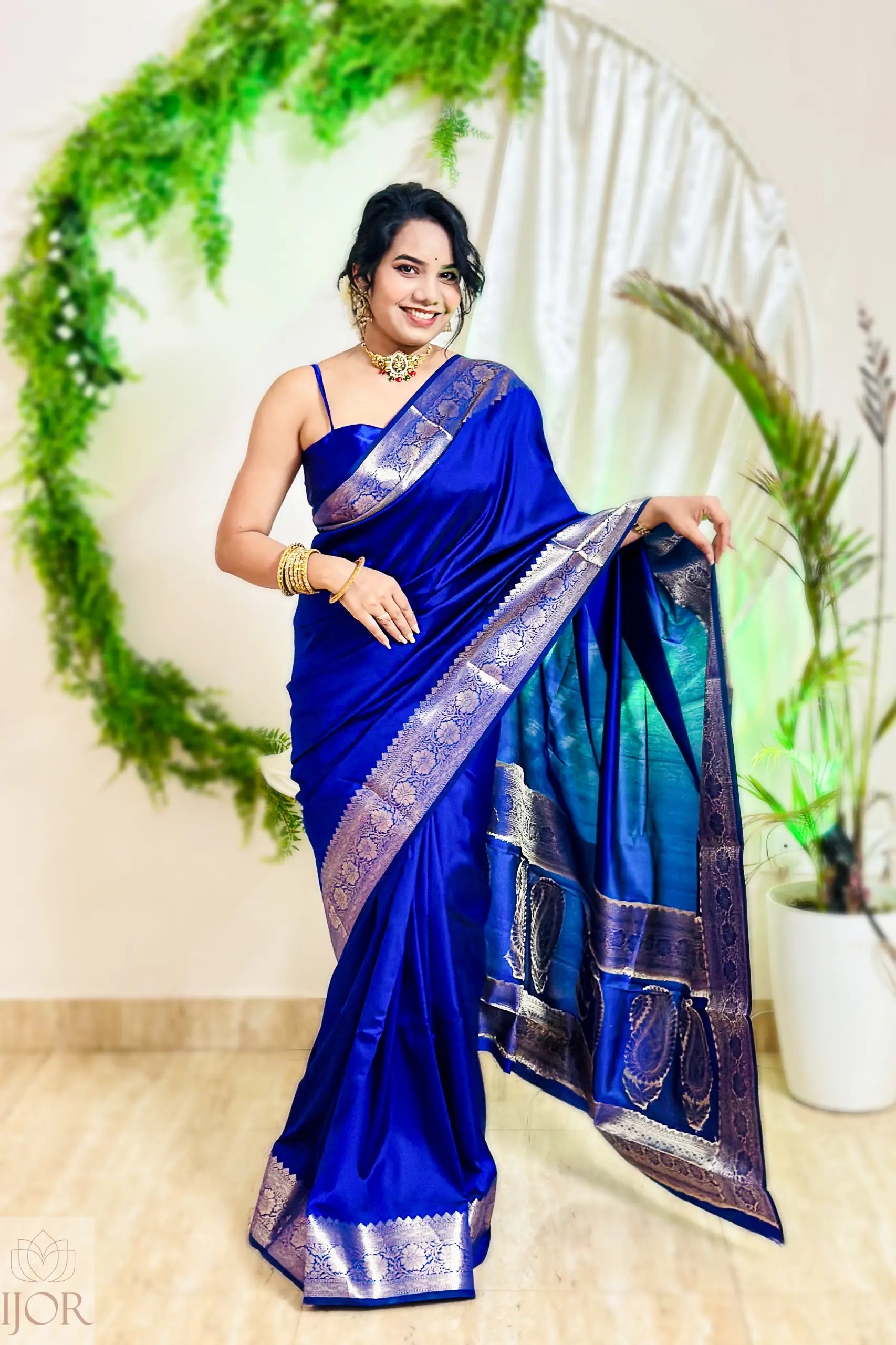 Woman in a blue saree with a decorative border standing in front of a decorative arch.