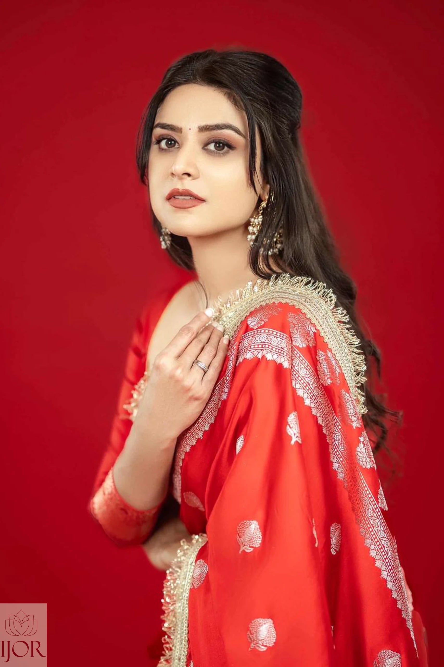 Woman in a Red Mashru Silk Saree with Maharani Lace with gold embroidery against a red background