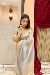 Woman in a Banarasi Silver Grey Tissue Silk Saree standing in front of a red curtain and framed mirror.