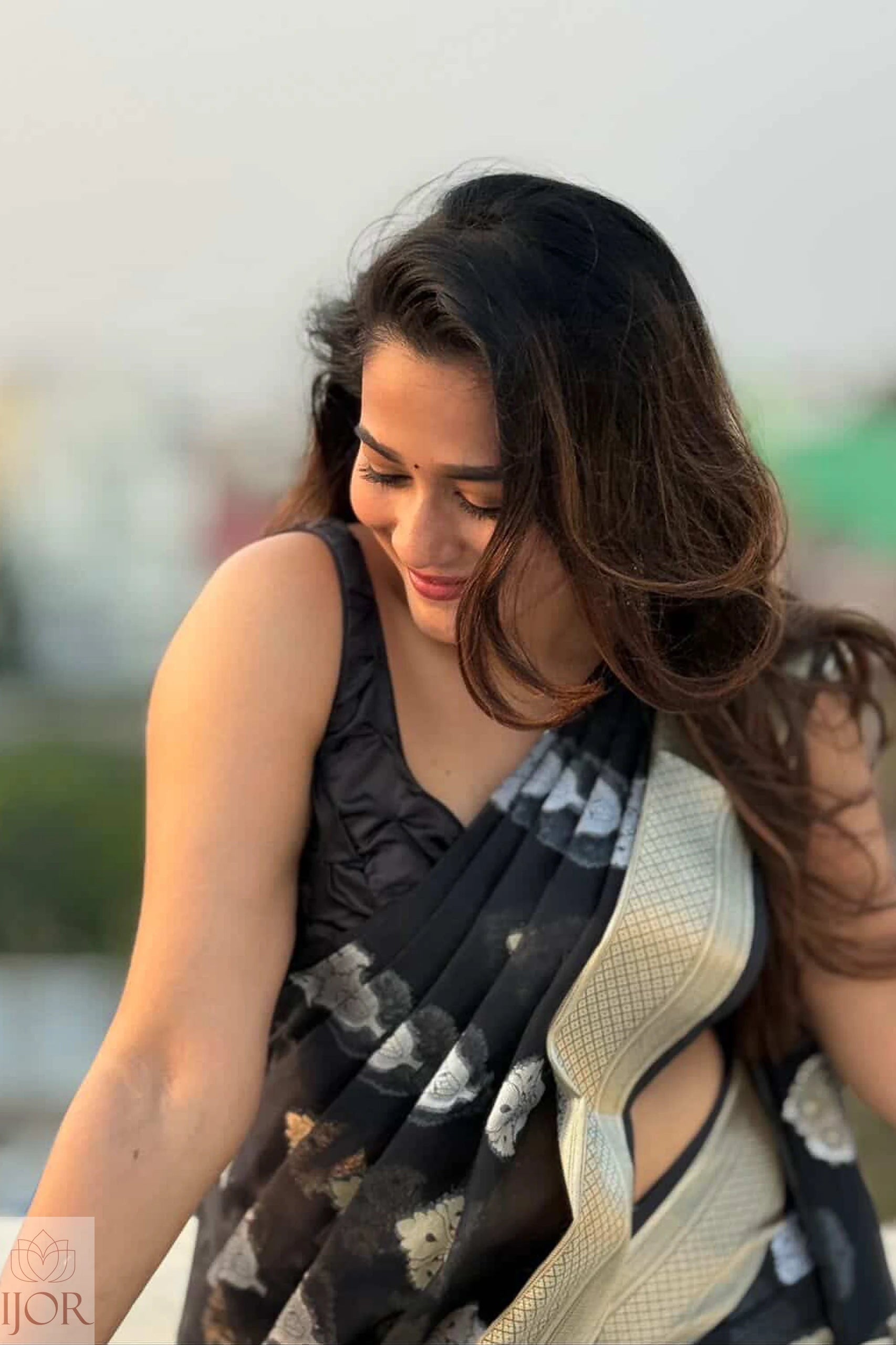 Kavya wearing a Kora Orgenza Silk Black Saree sitting outdoors with a blurred background