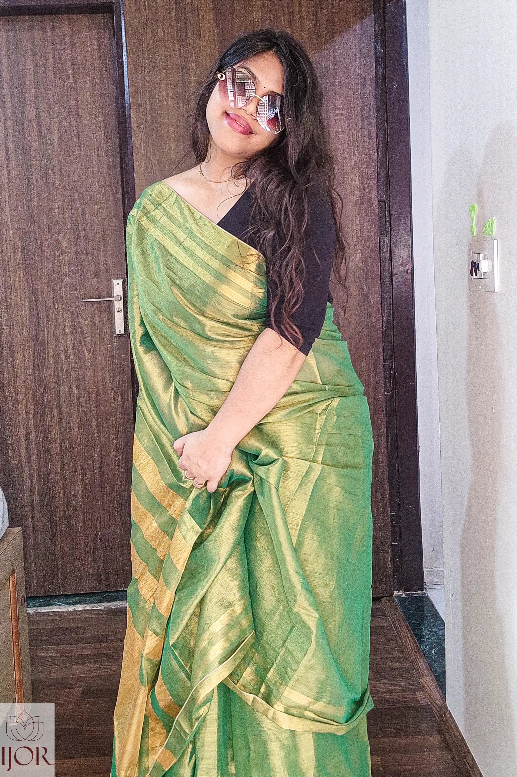   Aarti in Green Golden Zari Pure Tissue Cotton Saree with a black blouse standing indoors.