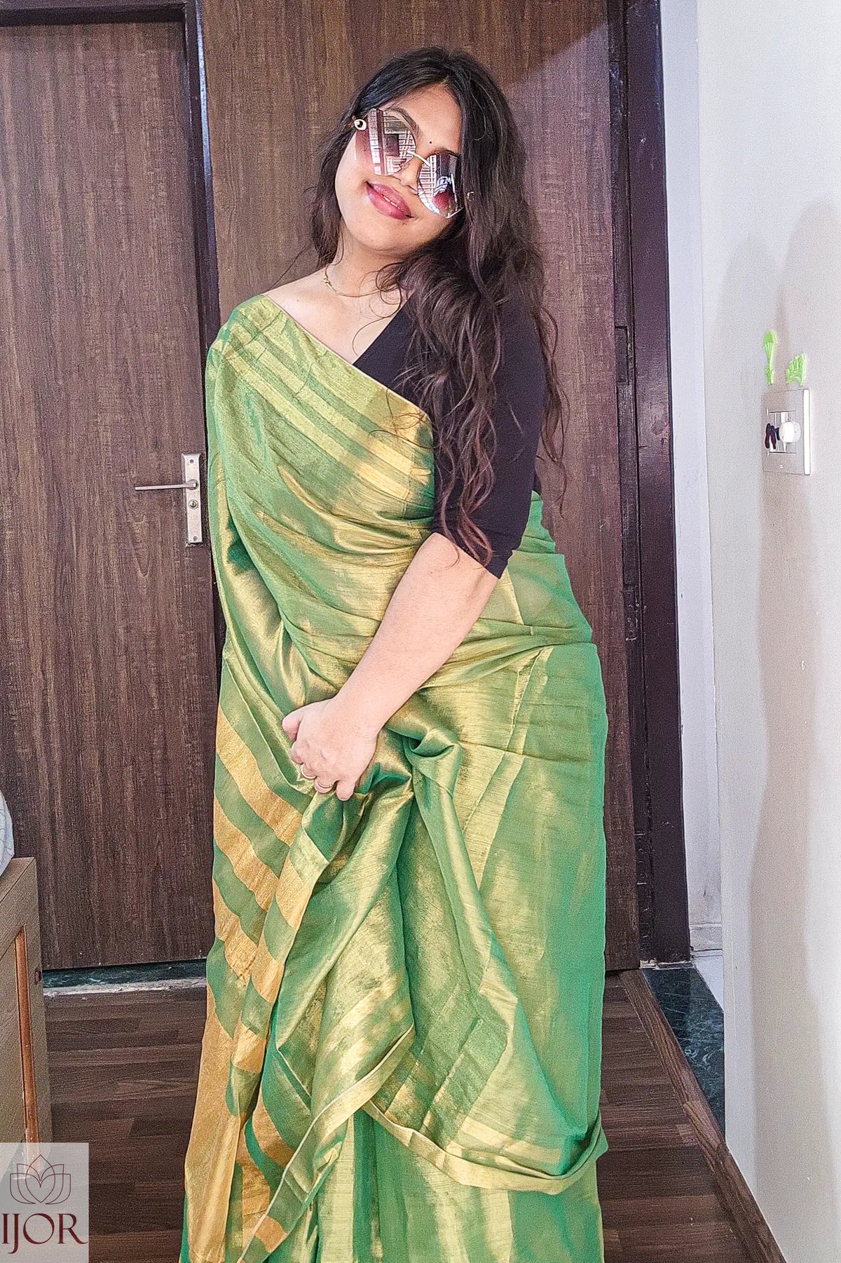   Aarti in Green Golden Zari Pure Tissue Cotton Saree with a black blouse standing indoors.