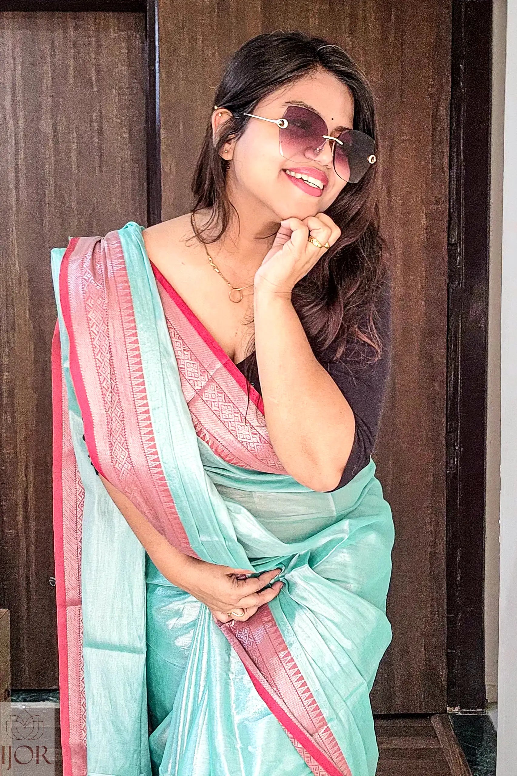 Woman wearing a Sea Foam Pure Tissue Cotton Saree with Rich Red Border indoors.