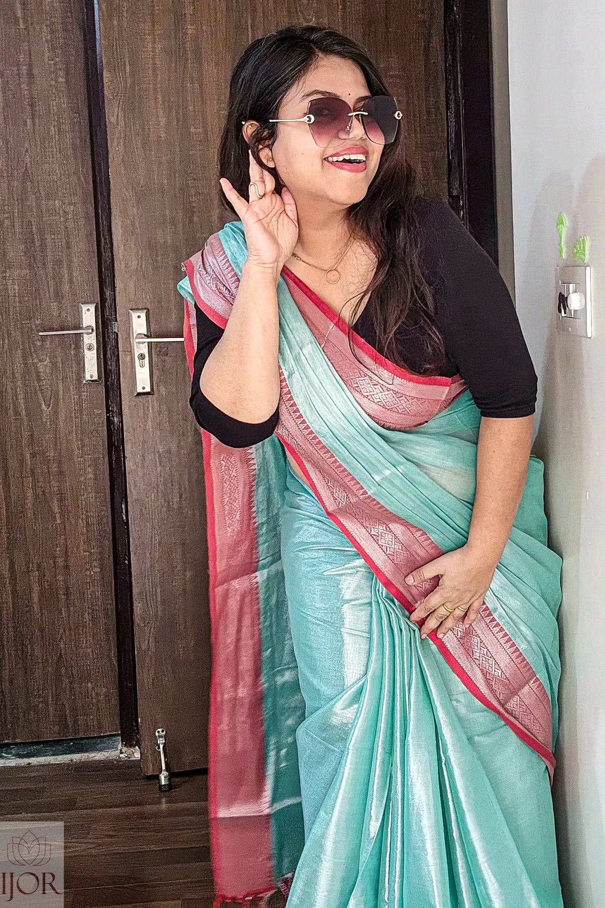 Woman wearing a Turquoise Blue Pure Tissue Cotton Saree with Rich Red Border indoors.